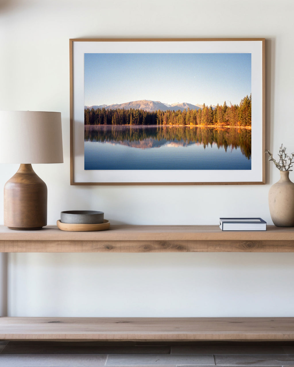Framed landscape print of a lake and mountains at Jasper national park on a wall above a wooden shelf with decor items.