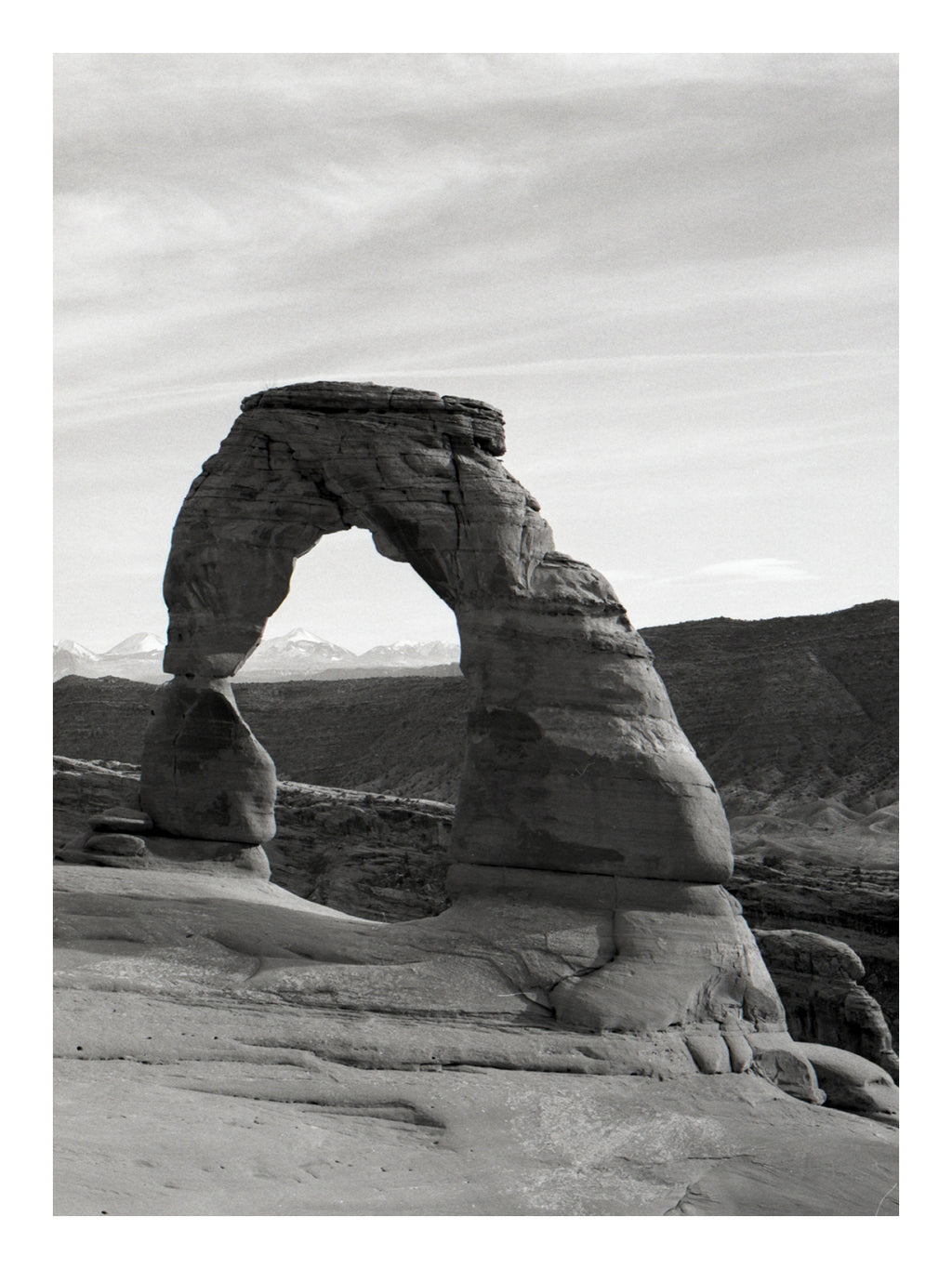 Black and white photograph of a large natural stone arch in a desert landscape in Arches np