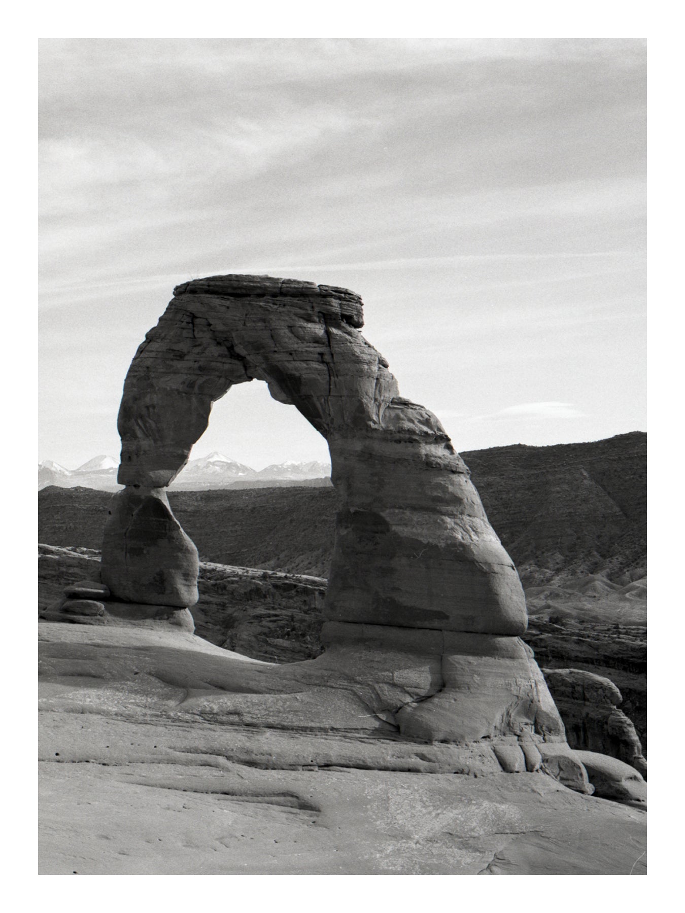 Black and white photograph of a large natural stone arch in a desert landscape in Arches np