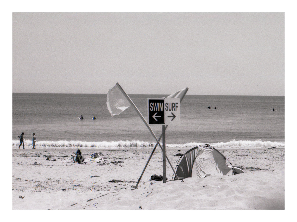 Beach scene with a tent, flags, and a swim surf sign in Malibu Beach California
