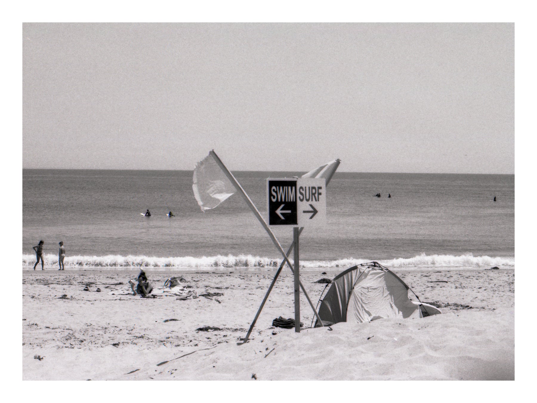 Beach scene with a tent, flags, and a swim surf sign in Malibu Beach California