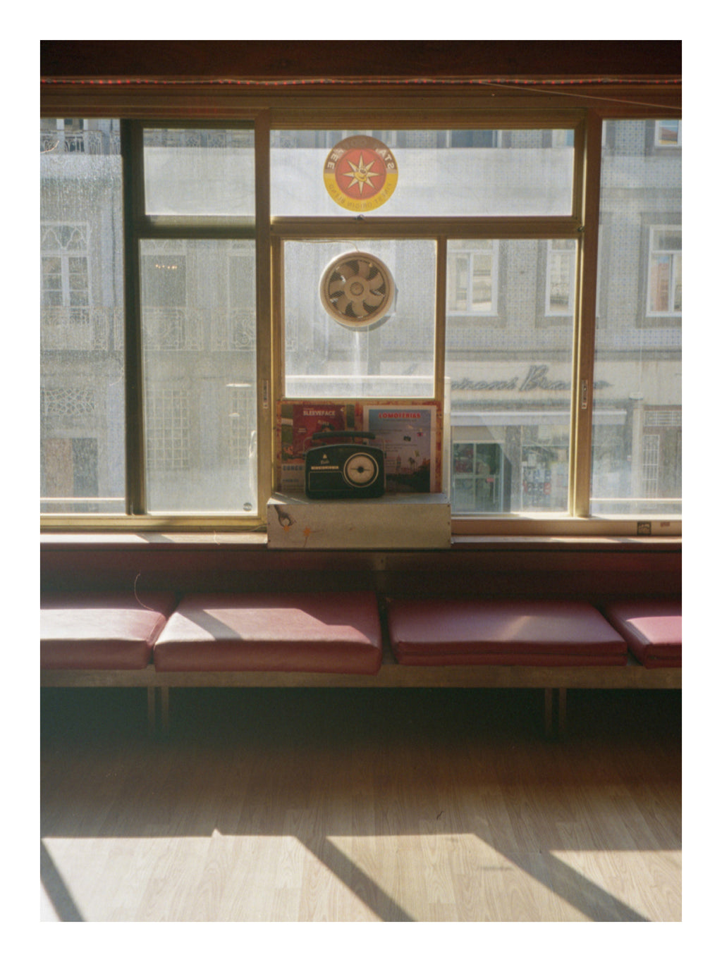 Bistro window with red cushioned seats and a clock on a sunny day in Portugal