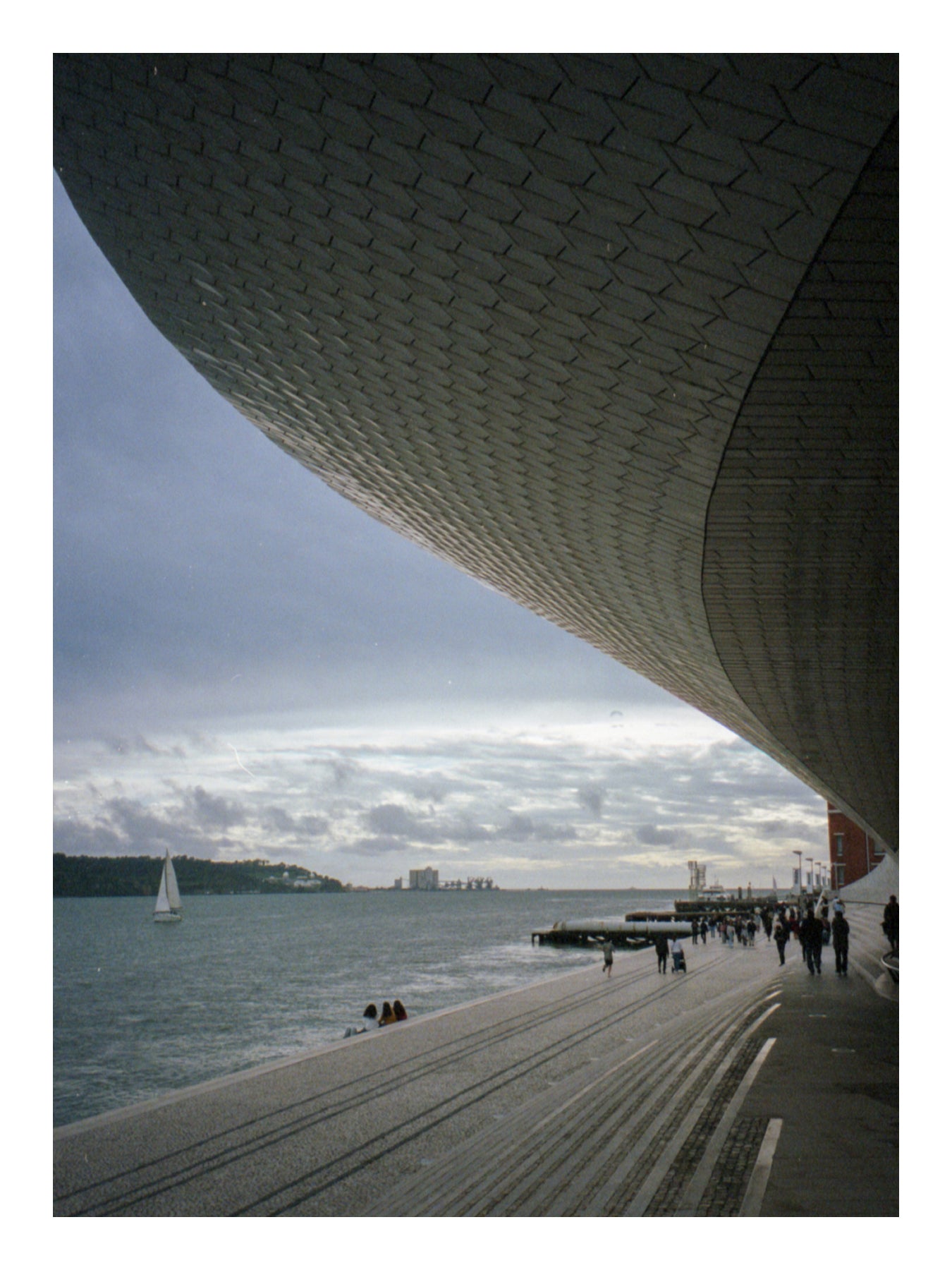 Modern architectural structure by a waterfront with people walking along a promenade in Lisbon, Portugal