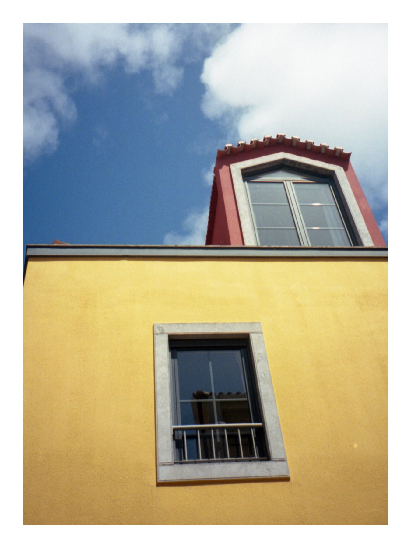 Yellow building facade with a red roof and two windows against a blue sky in Portugal