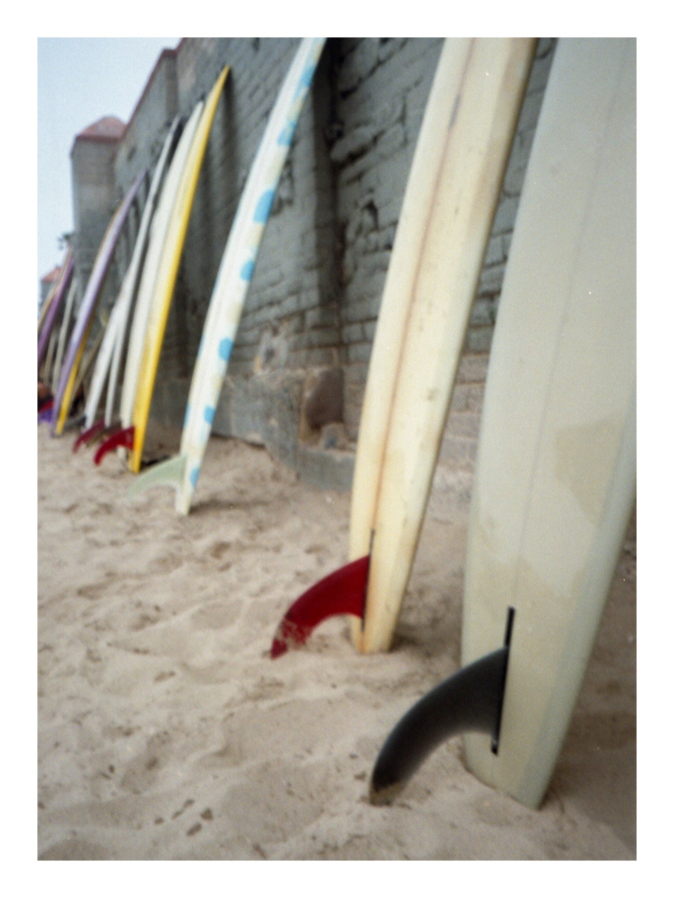 Surfboards leaning against a stone wall on a sandy beach. Malibu beach Surf days photo post cards