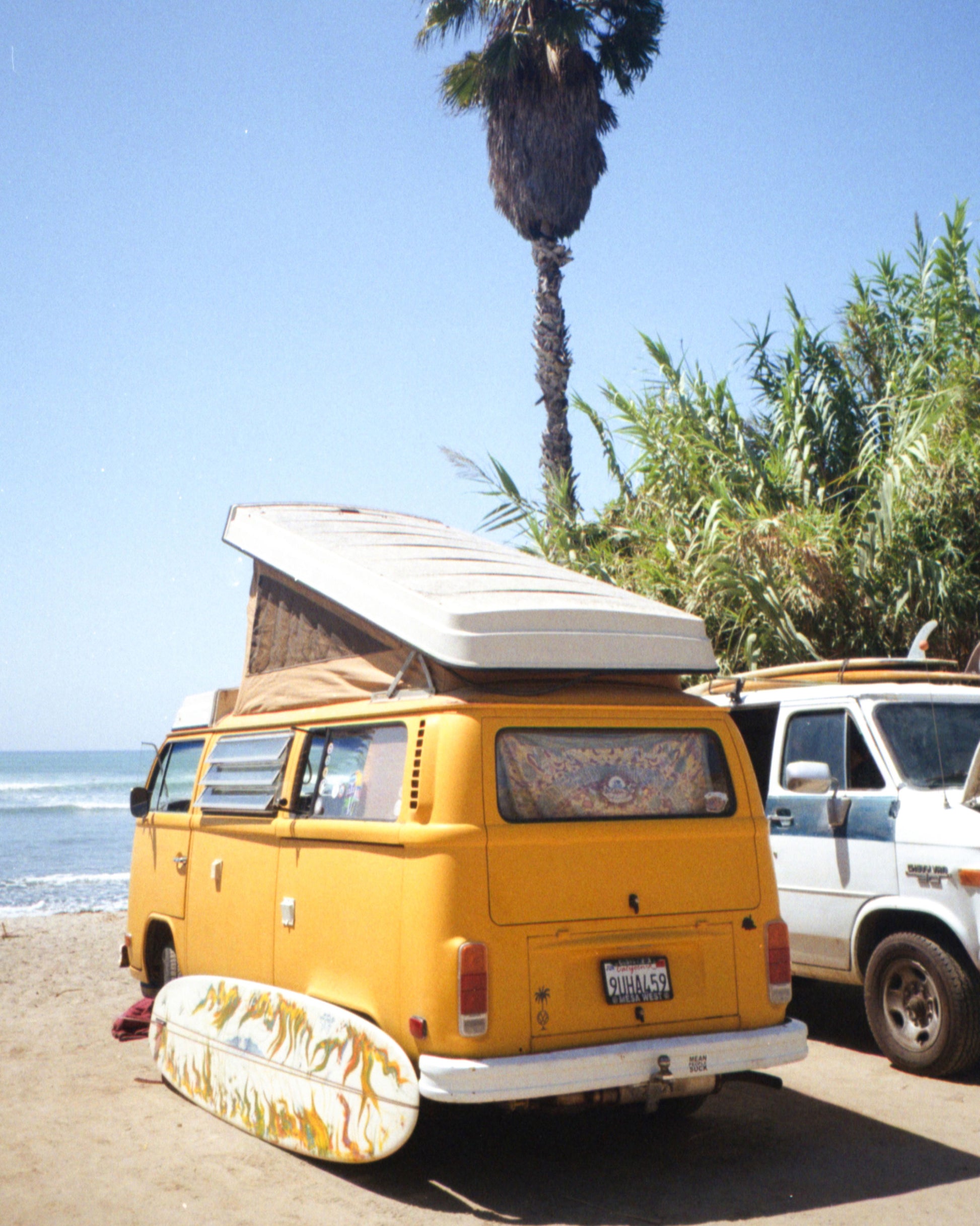 Yellow van with a surfboard on a beach with palm trees in the background