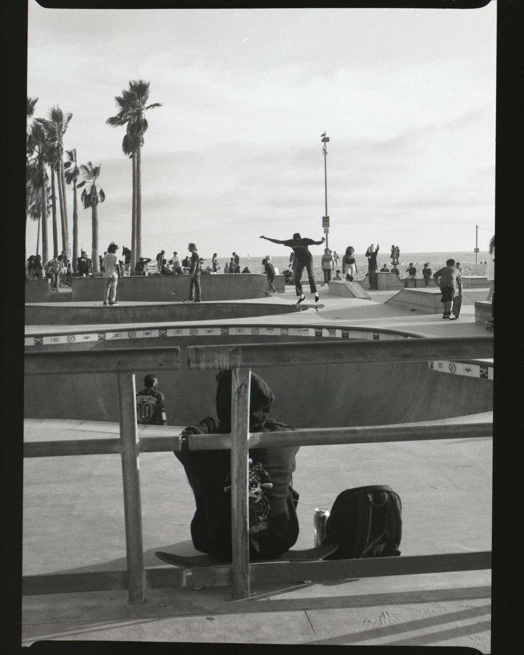 Skateboarder performing a trick at a venice beach skate park with onlookers in the background.
